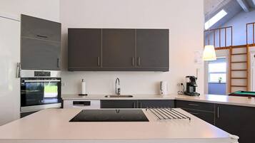 A modern kitchen with dark cabinets, a built-in oven, a sink, and a coffee machine.
