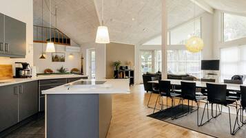 A modern kitchen with a central island, dining area with chairs, and a large window providing natural light.