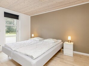 A bedroom with a large bed, two bedside tables, and a window with a view of greenery. - 10 Person Holiday Home in Vaeggerlose (Vaeggerlose)