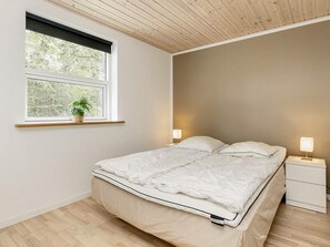 A bedroom with a bed, bedside tables, a window with a plant, and a wooden ceiling. - 10 Person Holiday Home in Vaeggerlose (Vaeggerlose)