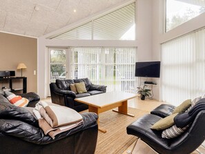 A modern living room with leather sofas, a wooden coffee table, a flat-screen TV, and large windows with blinds. - 10 Person Holiday Home in Vaeggerlose (Vaeggerlose)