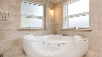 A modern bathroom with a freestanding bathtub, two windows, and a wooden ceiling.