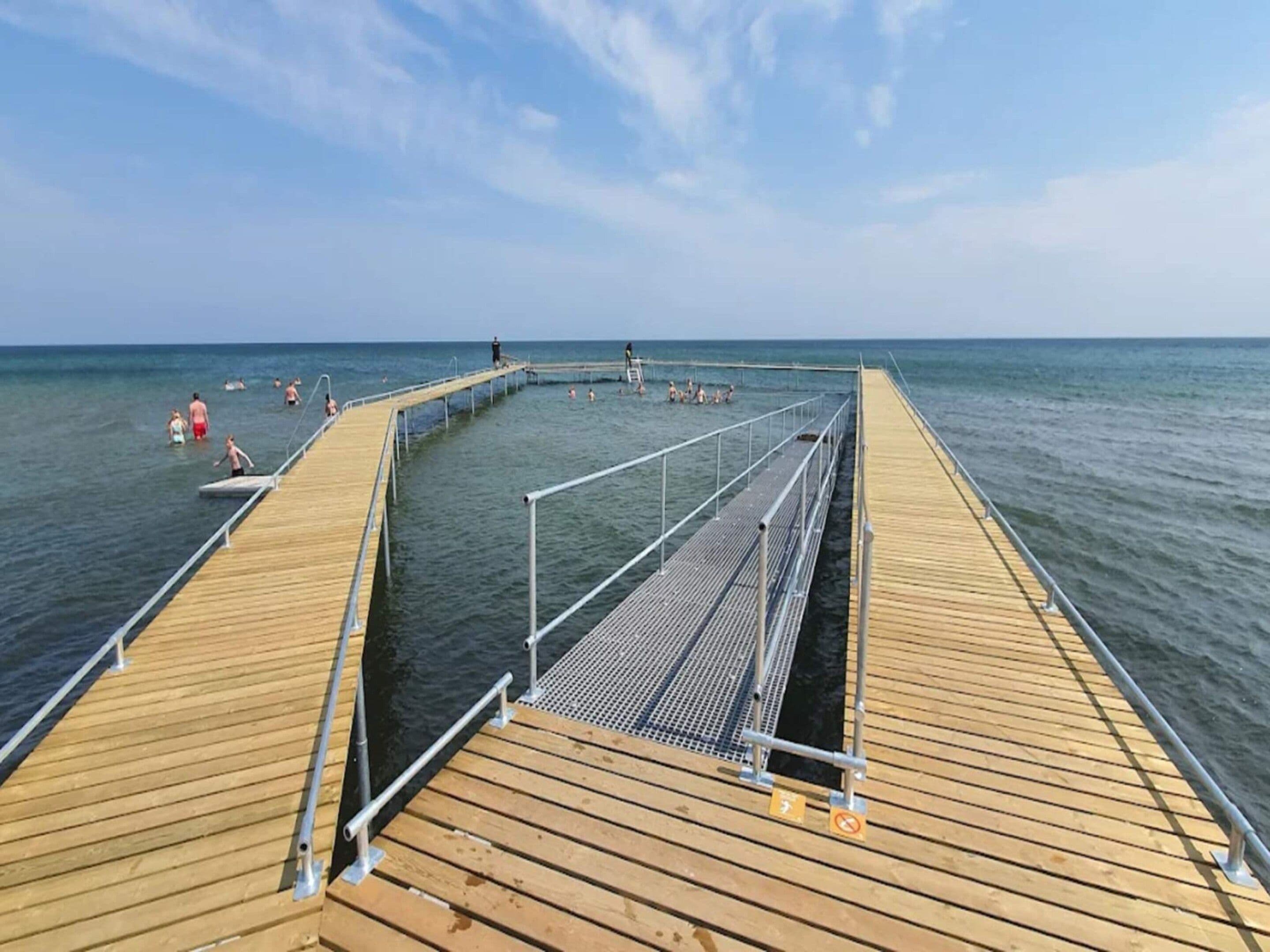 A wooden pier extending into the sea with people swimming and walking.