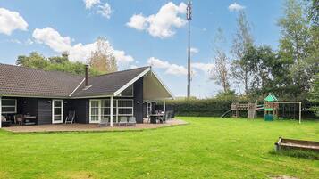 A building with a sloped roof and large windows, adjacent to a grassy area with a playground.