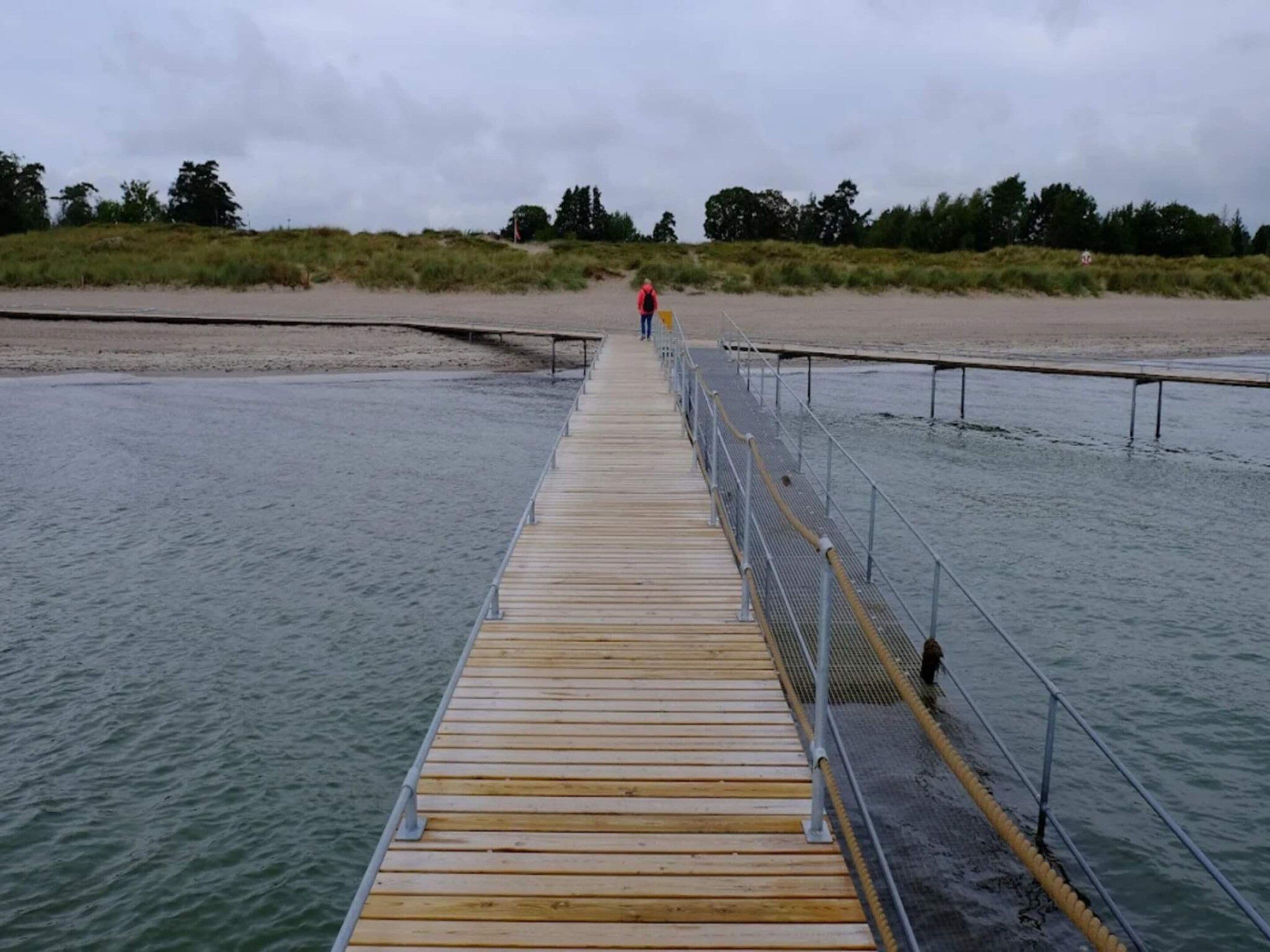 A wooden pier extending into a body of water with a metal railing on one side.