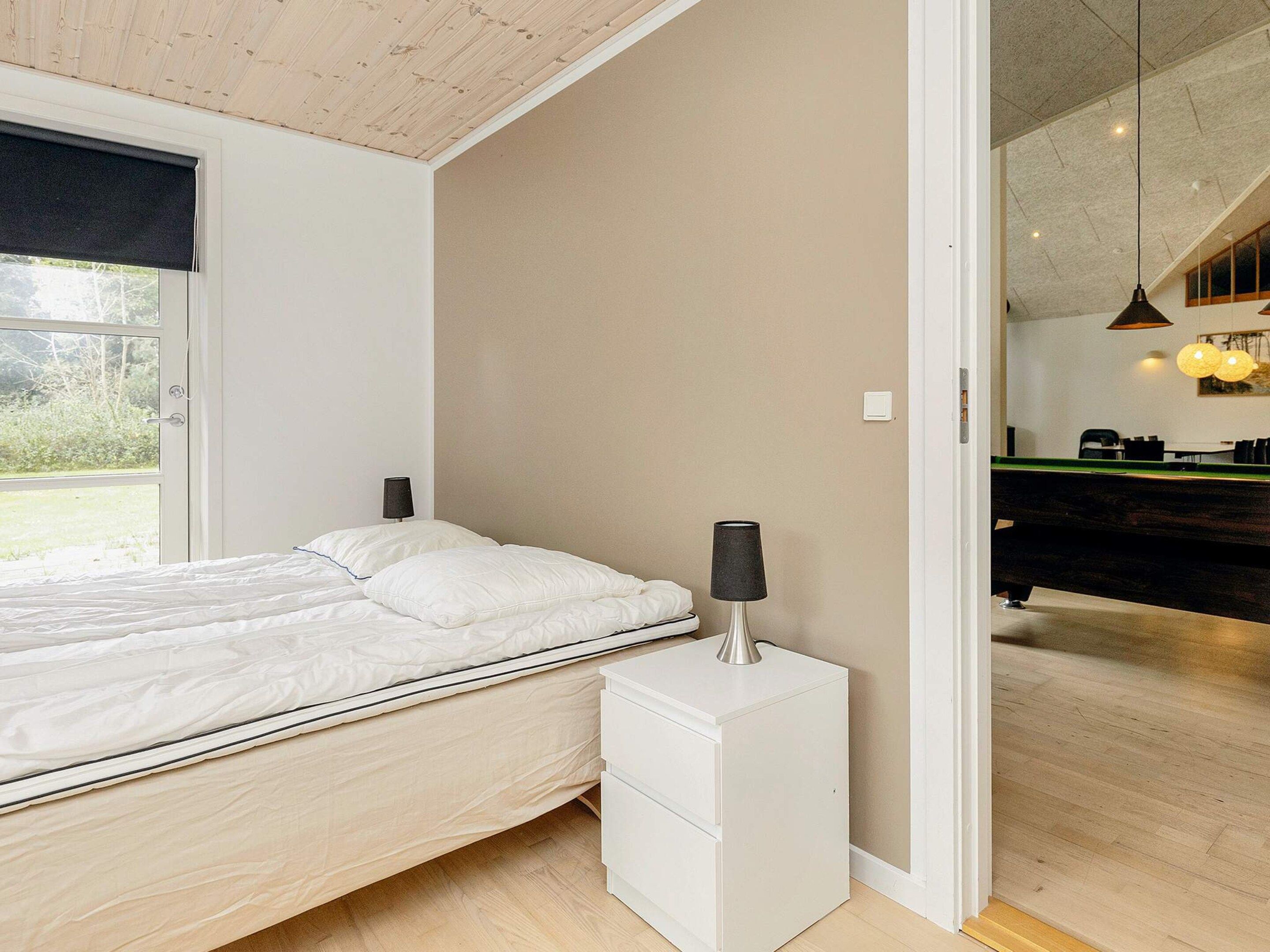 A bedroom with a bed, bedside lamp, and a view of a dining area.