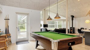 A pool table in a room with a fireplace, wicker furniture, and a view through large windows. - 10 Person Holiday Home in Vaeggerlose (Vaeggerlose)
