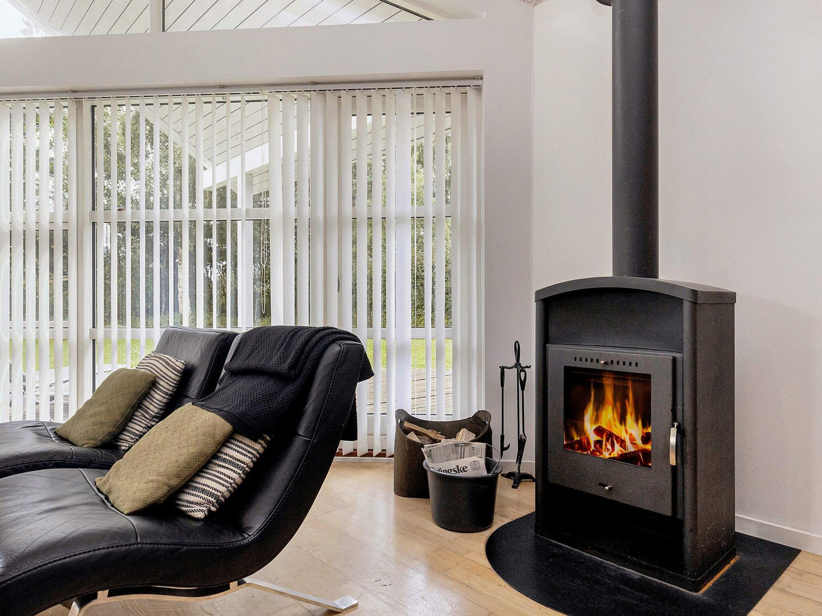 Ein modernes Wohnzimmer mit einer schwarzen Ledersofa, einem Kamin und Blick durch große Fenster.