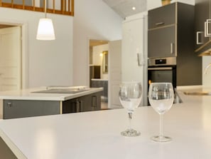 A modern kitchen with a white countertop, two wine glasses, and a hanging pendant light. - 10 Person Holiday Home in Vaeggerlose (Vaeggerlose)