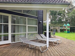 A covered outdoor area with a wooden deck, two lounge chairs, and a children's play structure. - 10 Person Holiday Home in Vaeggerlose (Vaeggerlose)