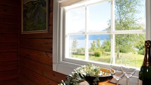 L'intérieur d'un chalet en bois, avec une grande fenêtre donnant sur un lac et la verdure environnante.