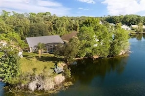 A house with a large deck overlooking a lake, surrounded by dense trees and a clear sky. - Lakeside Sunset 3 Bedroom by RedAwning (Davenport)