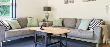 Ein Wohnzimmer mit einem grauen Sofa, einem Holztisch und zwei Bildern an der Wand.
