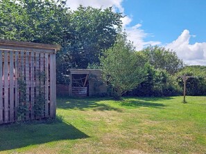 A fenced garden area with a wooden structure, a small shed, and dense shrubbery.