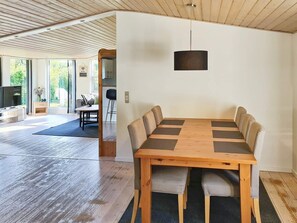 A modern dining area with a wooden table and chairs, a hanging pendant light, and a view of the outdoors through large windows.