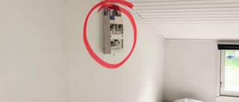 A room with a white ceiling, a window on the right, and a wall-mounted electrical box circled in red.