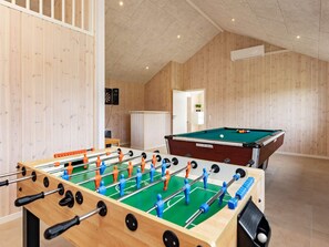Una habitación con mesa de fútbol de mesa, mesa de billar y paneles de madera en las paredes.