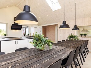 A modern kitchen with white cabinets, a wooden dining table, and black pendant lights.