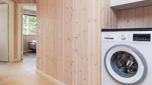 Un lavadero con lavadora Siemens, paredes de madera y vista hacia un dormitorio.