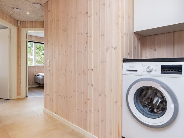 Une buanderie équipée d’un lave-linge Siemens, avec des murs en bois et une vue sur une chambre.