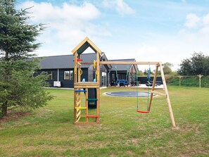 Une structure de jeu en bois avec un toboggan et des balançoires, installée dans une cour gazonnée.