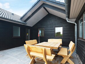 A wooden outdoor seating area with a table and benches, a black exterior wall, and a tiled roof. - 20 Person Holiday Home in Hojslev (Hojslev)
