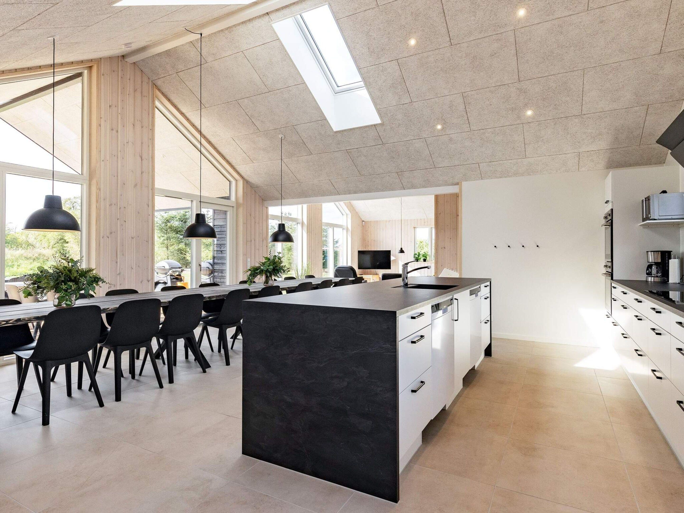 A modern kitchen with a large island, black pendant lights, and a dining area with chairs and a table.