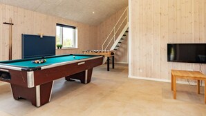 Una mesa de billar junto a una mesa de futbolín y un televisor en una sala con paredes de madera y una escalera.