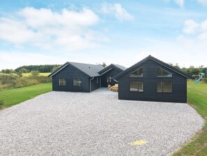 A modern two-story house with a gravel driveway, a wooden deck, and a playground in the background. - 20 Person Holiday Home in Hojslev (Hojslev)