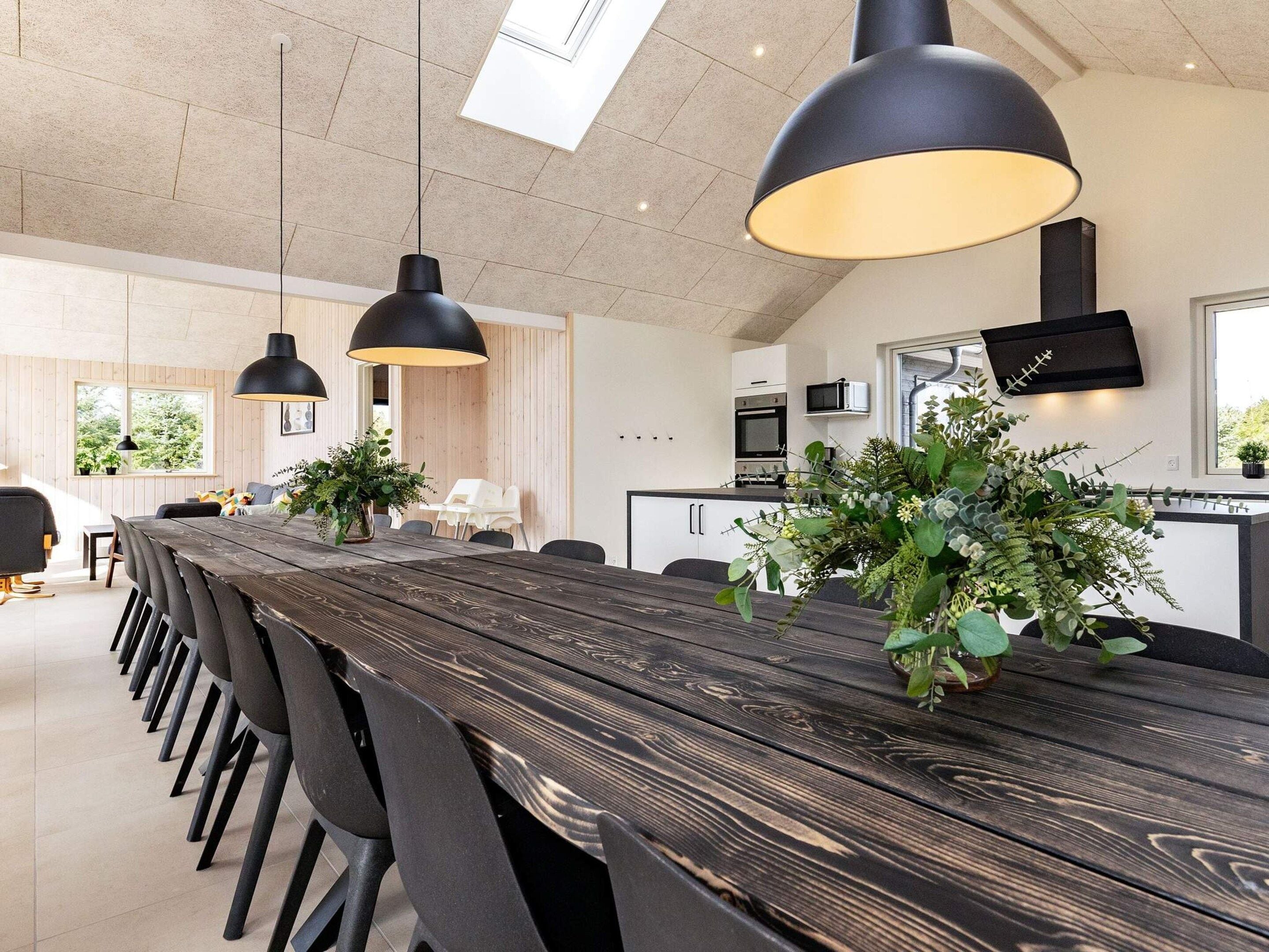 A modern dining area with a long wooden table, black chairs, and pendant lighting.