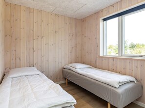 Una habitación con dos camas individuales, paredes de madera, una ventana con persianas y vistas a zonas verdes.