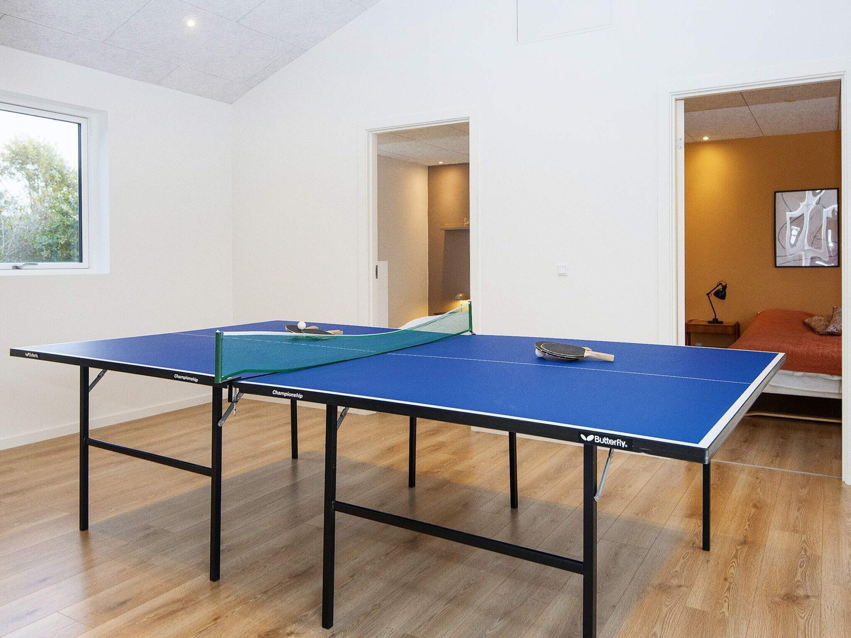 A ping pong table in a room with wooden flooring and a window.