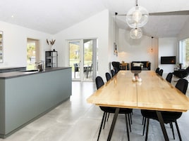 Una cocina moderna con una isla grande, un comedor con una mesa larga y una sala de estar con televisor.