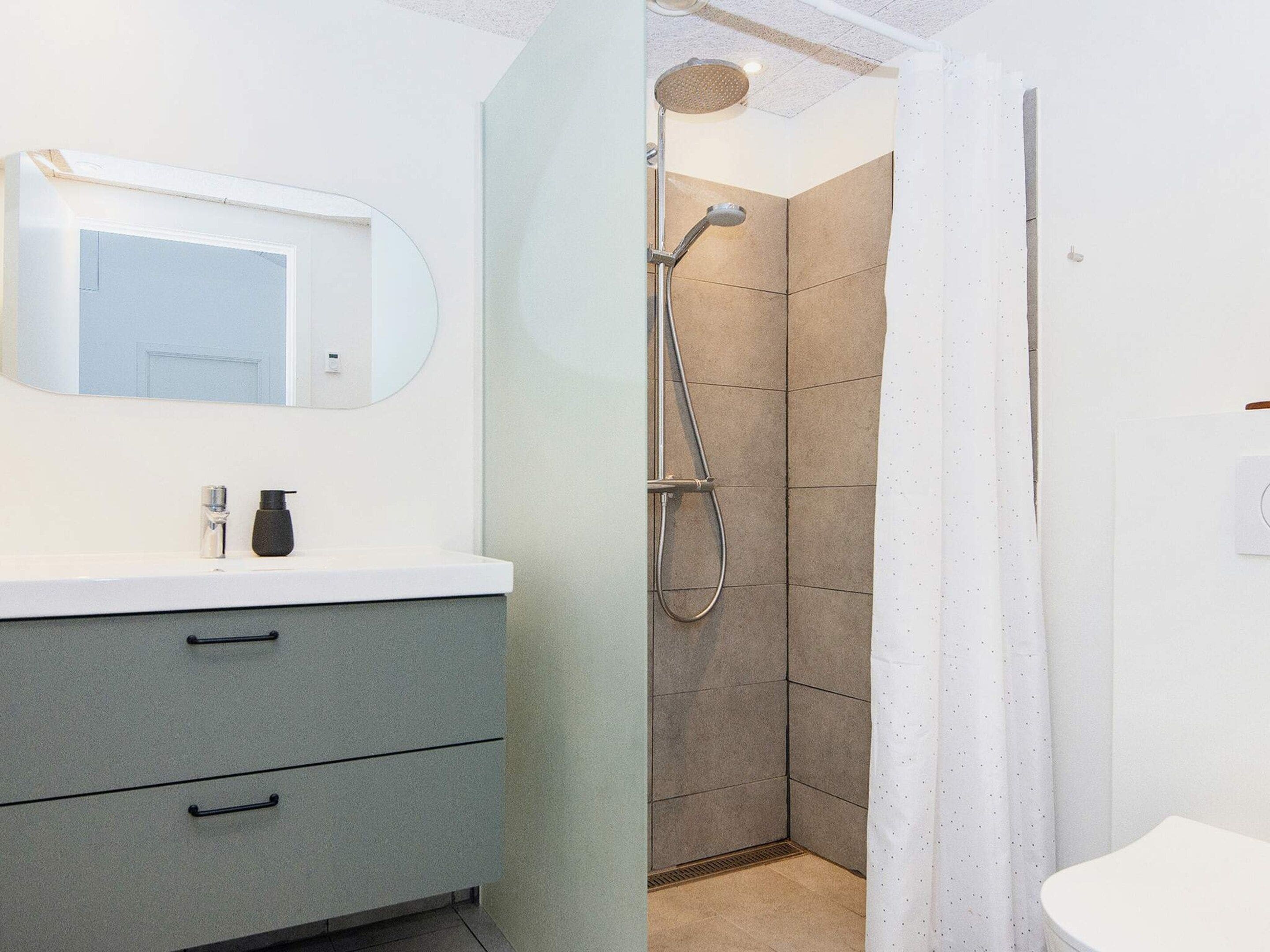Et badeværelse med brusebad, vask med spejl og toilet.