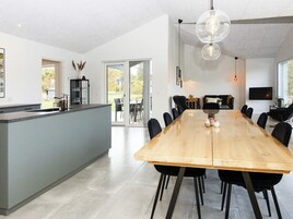 Una cocina moderna con una isla grande, un comedor con una mesa larga y un espacio de sala con sofá y televisor.