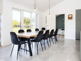 Un comedor moderno con una mesa larga, sillas negras y lámparas colgantes.