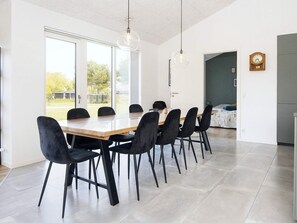 Un espace de restauration moderne, doté d’une longue table et de chaises, de grandes fenêtres et offrant une vue sur l’extérieur.