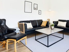 Una sala moderna con un sofá de cuero negro, una silla de madera y una mesita de centro.