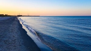 A beach with a calm sea, a clear sky, and distant structures.