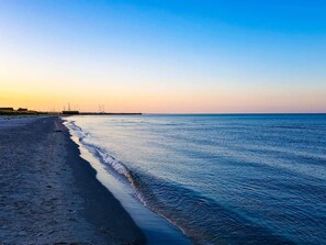 Uma praia com mar calmo, céu claro e construções ao longe.