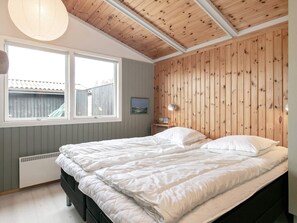 Un dormitorio con una cama, dos mesitas de noche, un ventanal y un panel de pared de madera.