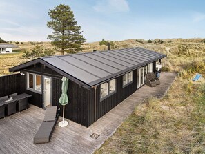 Une cabane noire dotée d’une terrasse, de sièges extérieurs et d’une chaise suspendue.