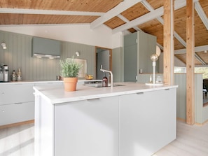 A modern kitchen with a central island, wooden beams on the ceiling, and a large window. - 5 Star Holiday Home in Albaek (Aalbaek)