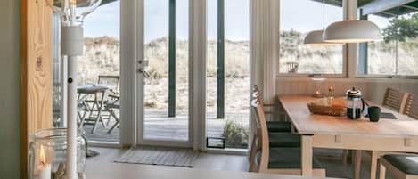 A modern kitchen with a large island, a dining area with a wooden table, and a view of the beach through large sliding doors.