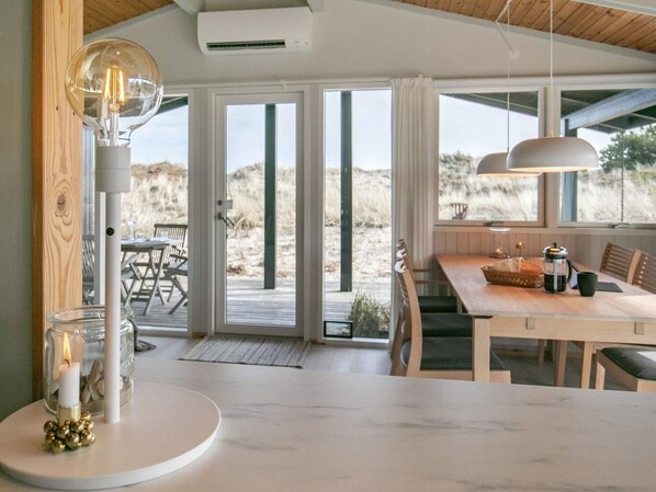 A modern kitchen with a large island, a dining area with a wooden table, and a view of the beach through large sliding doors.