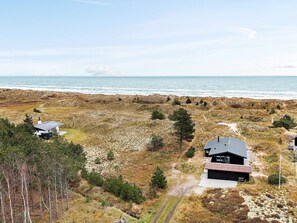 A coastal landscape with two modern houses, one with a sloped roof and the other with a flat roof, surrounded by natural terrain and a view of the sea. - 5 Star Holiday Home in Albaek (Aalbaek)