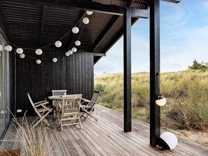 A wooden deck with a table and chairs, surrounded by a black wall and string lights. - 5 Star Holiday Home in Albaek (Aalbaek)