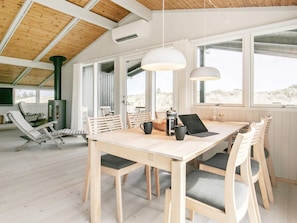 A spacious room with a wooden table and chairs, a fireplace, and large windows offering a view of the outdoors. - 5 Star Holiday Home in Albaek (Aalbaek)