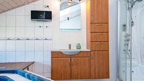 A bathroom with a shower, a sink with a mirror, and a wooden cabinet. - 4 Star Holiday Home in Tarm (Hemmet)