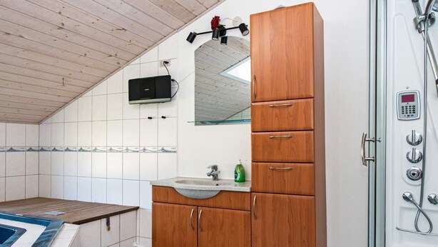 A bathroom with a wooden vanity, a sink, a mirror, and a shower enclosure. - 4 Star Holiday Home in Tarm (Hemmet)